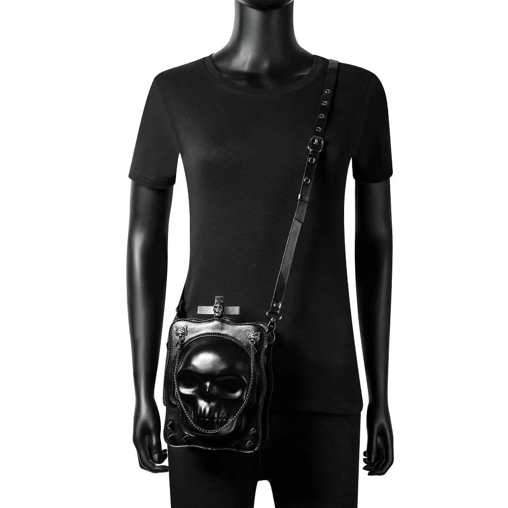 Black vertical square mini crossbody bag with embossed skull design, metal rivets, and chain strap.