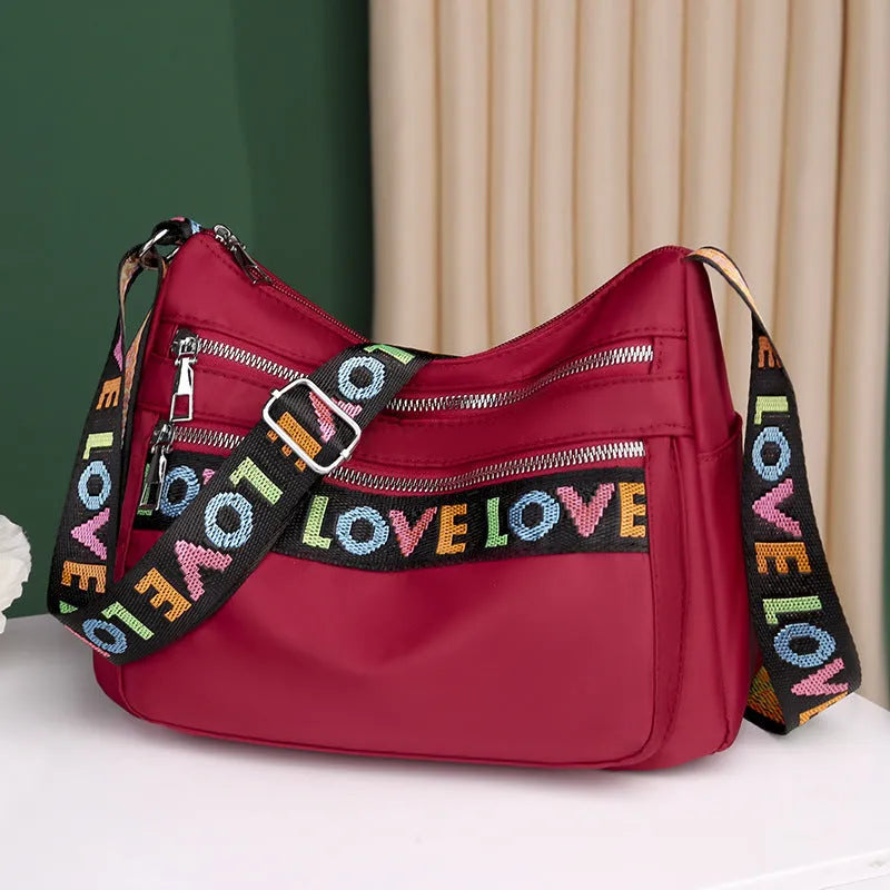 Oxford cloth crossbody shoulder bag in red or black with multi-pocket design, single strap, polyester lining, and letter stitching detail.
