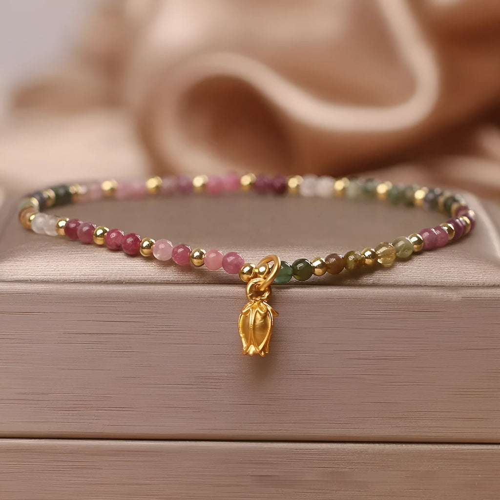 Close-up of a women's beaded anklet with polished tourmaline stones and a detailed metal floral clasp.