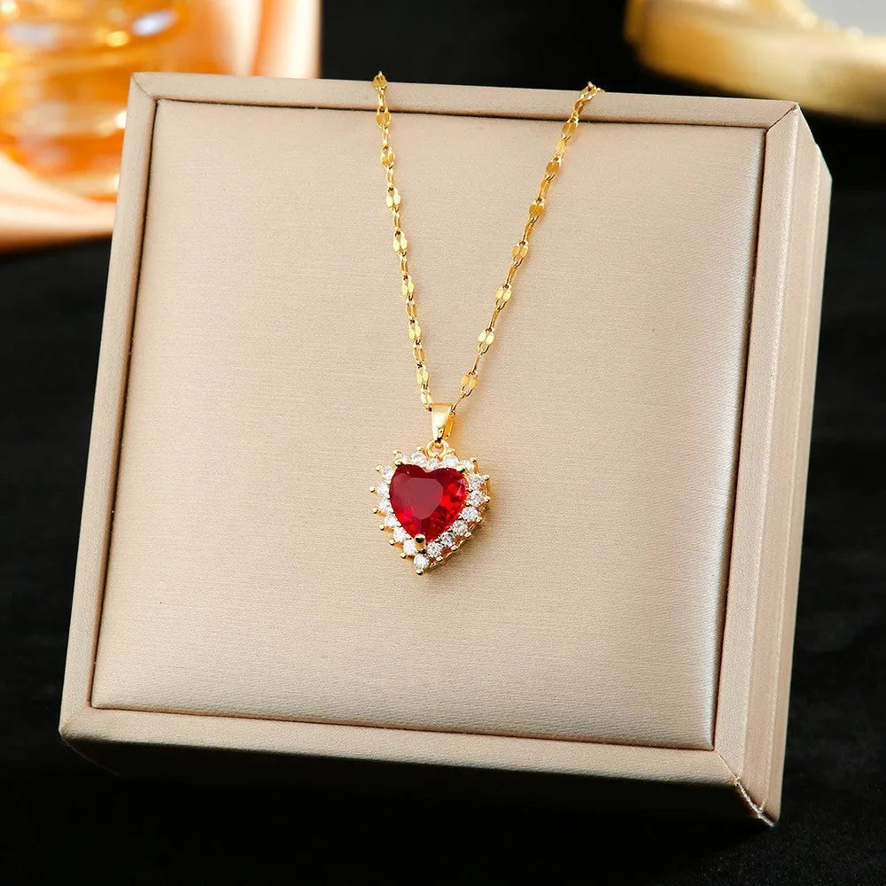 Gold red titanium steel necklace with heart and flower gemstone pendant, matching stud earrings, and ring on a jewellery stand.
