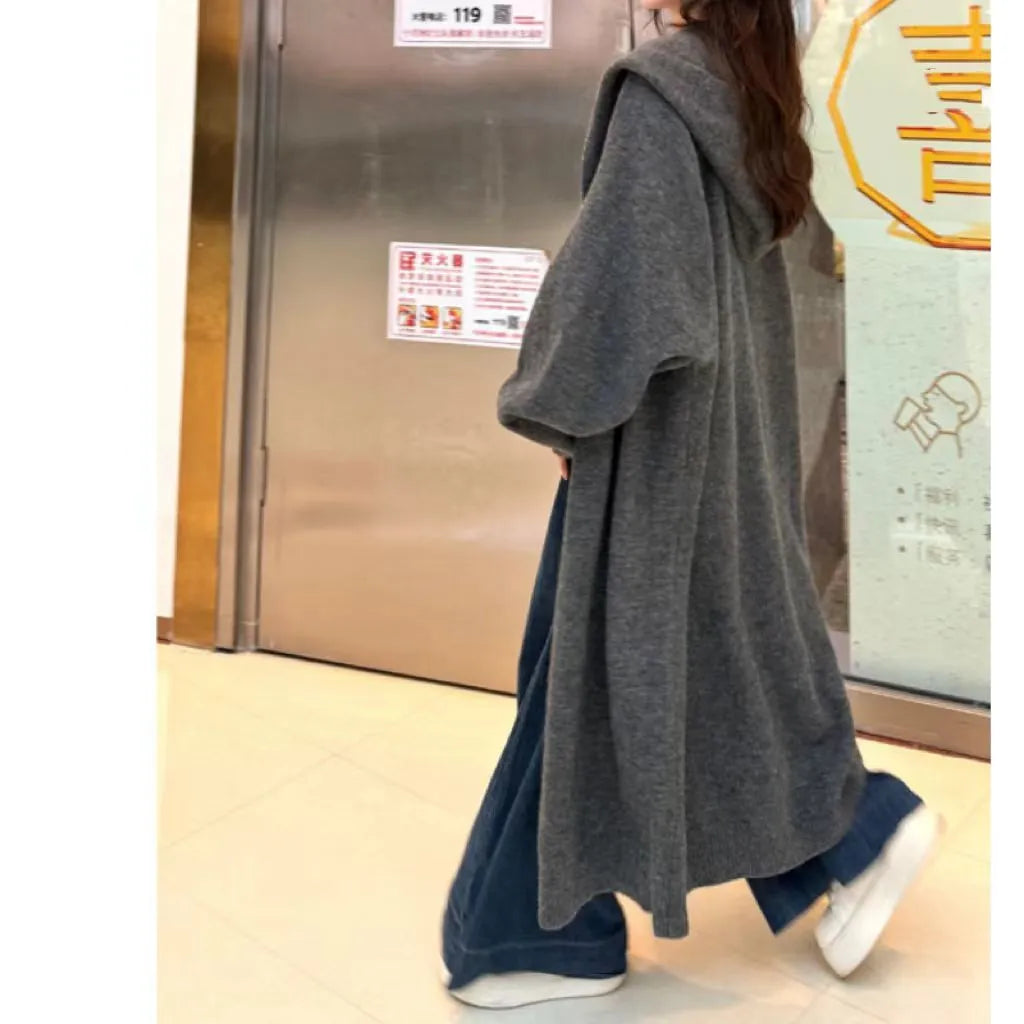 A woman wearing a long, loose, hooded knitted cardigan in a solid colour, demonstrating its below-the-knee length.