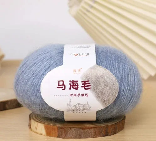 A ball of mohair yarn in a selected colour next to a hand-woven scarf example, showcasing the DIY kit.