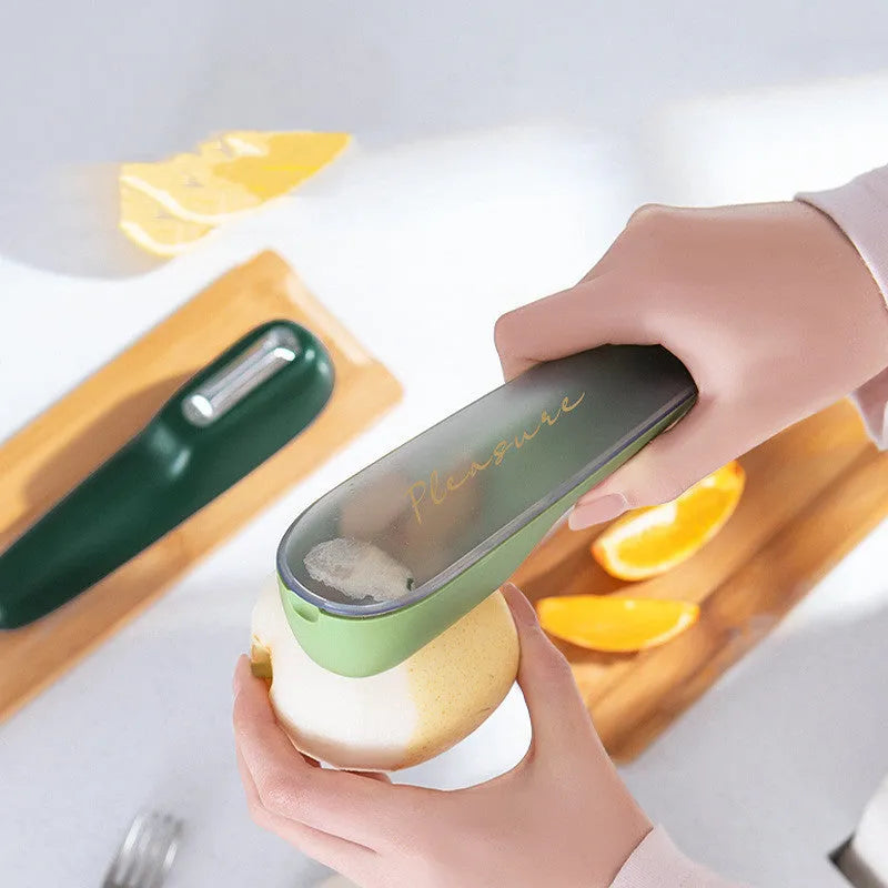 Dark green kitchen peeler with a storage tube extended, showing the stainless steel blade and a hanging hole on the handle.