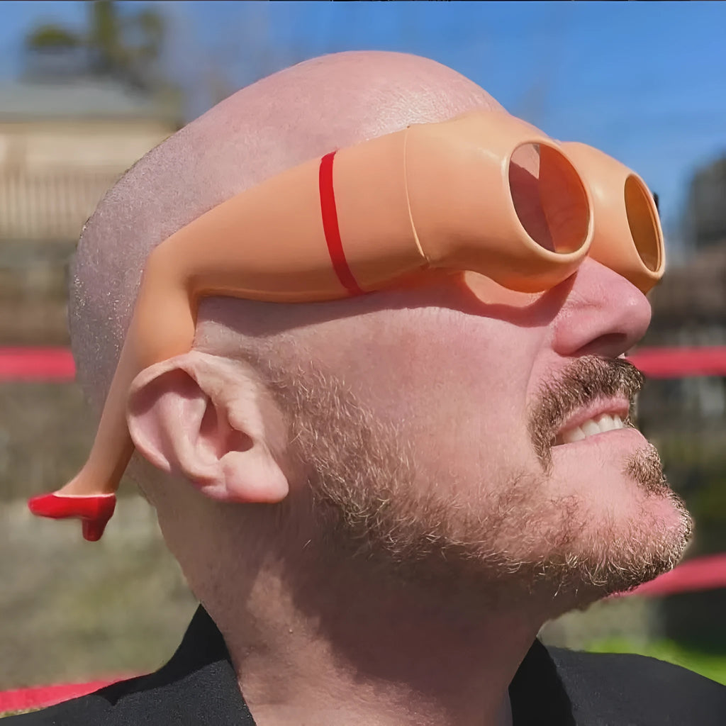 Orange novelty sunglasses with a unique leg-hip frame design, shown from the front. Oversized 15cm by 20cm dimensions.