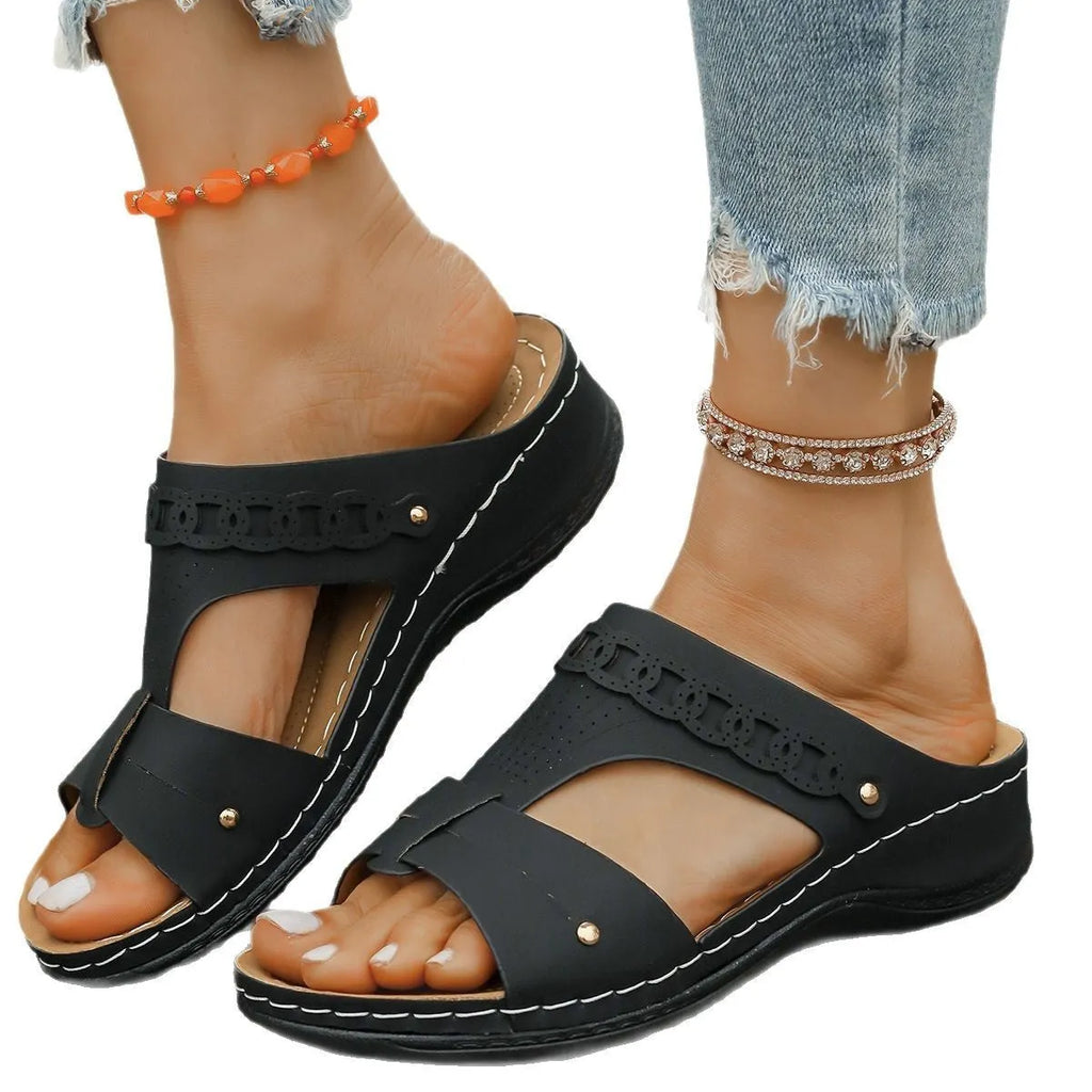 Pair of beige Roman style slippers with a fish mouth toe holder and slope heel on a rubber sole.