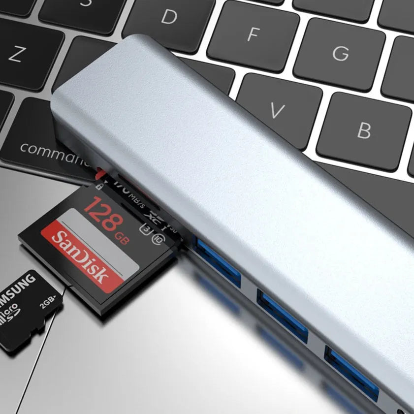 Silver seven-port type-C USB expander hub with a short black cable on a wooden desk.
