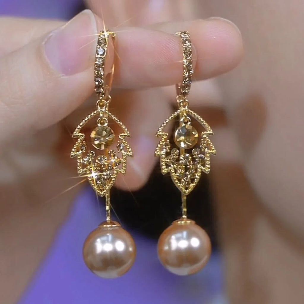 Coffee-coloured metal leaf earrings with full diamond-cut surface and pearl accents, old money style, side view on white background
