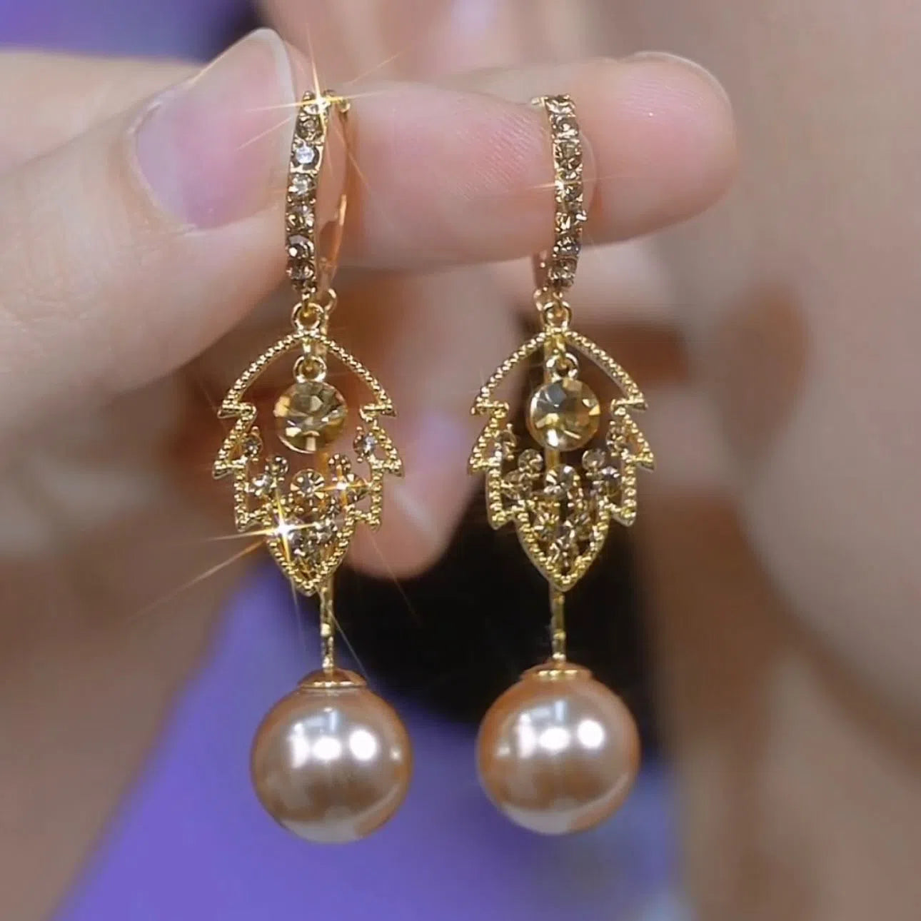 Coffee-coloured metal leaf earrings with full diamond-cut surface and pearl accents, old money style, side view on white background