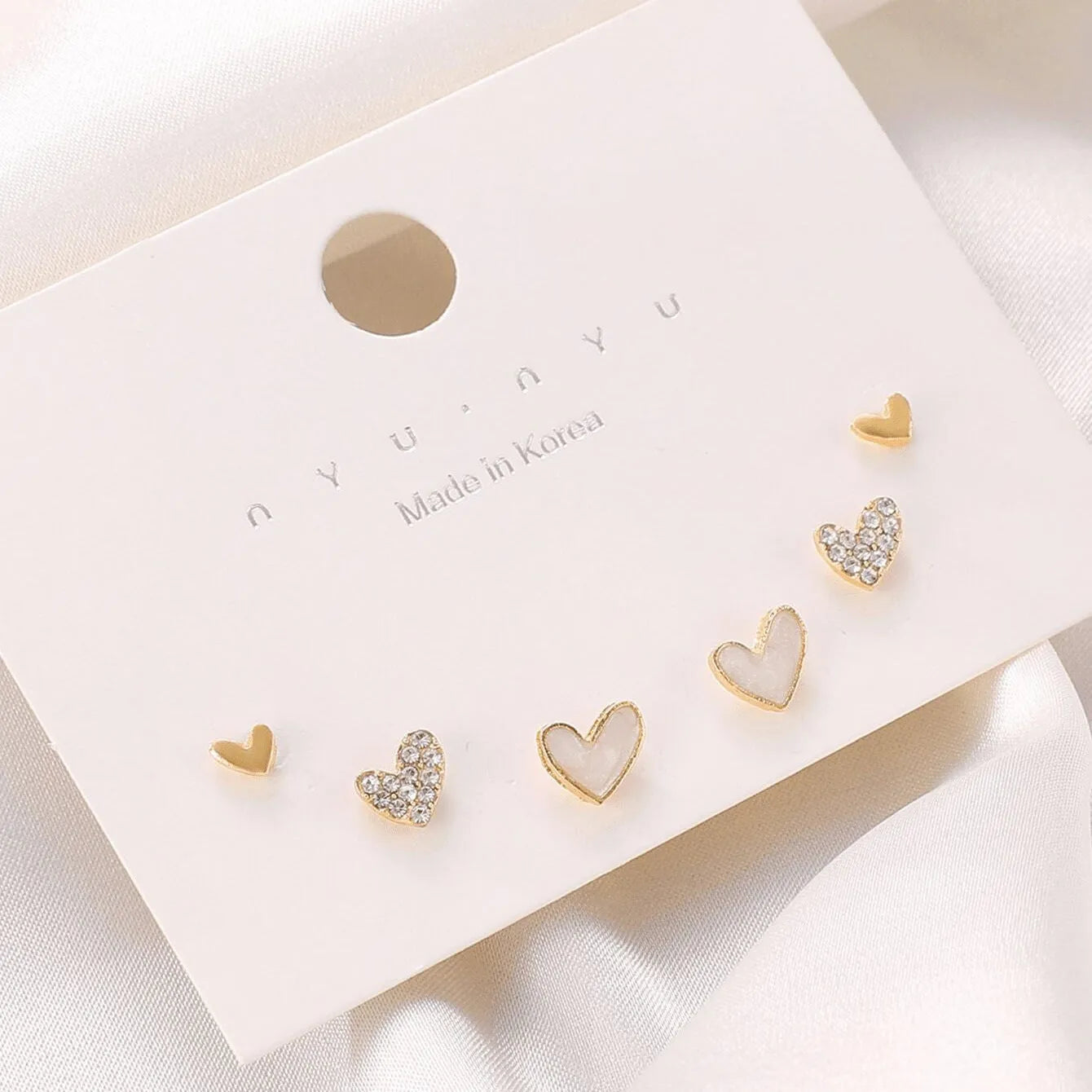 Three pairs of heart-shaped alloy earrings in gold, black, black and white, and pink colours on display.