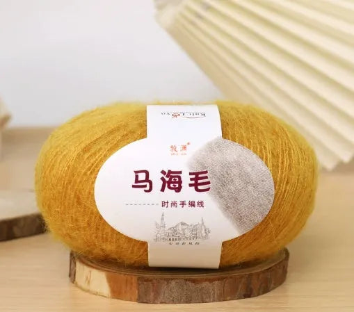 A ball of mohair yarn in a selected colour next to a hand-woven scarf example, showcasing the DIY kit.