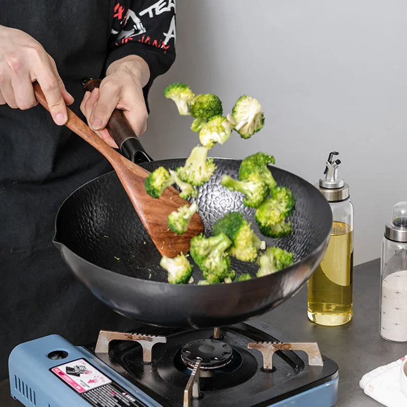 Handmade traditional black cast iron wok with wooden handle on a kitchen counter.