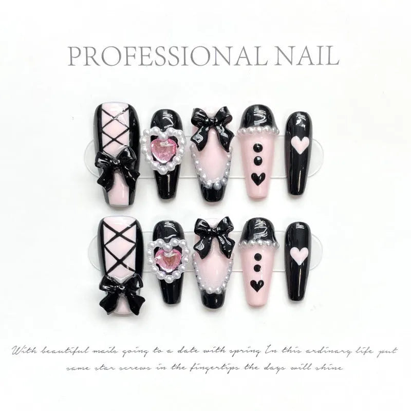 Black false nails with pink hand-painted peach hearts and bow design, shown in a cat's eye style.