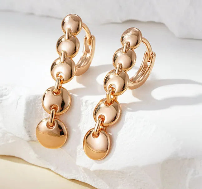 A pair of long, round, woven copper earrings with a gold finish, showing textured detail.