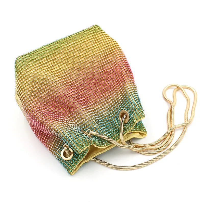 Soft rainbow iridescent bucket bag covered in sparkling rhinestones with a shoulder strap on a white background.