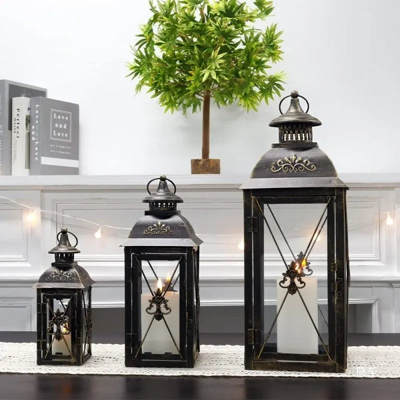 Black and white wrought iron floor-standing storm lantern with tempered glass panels in three sizes.