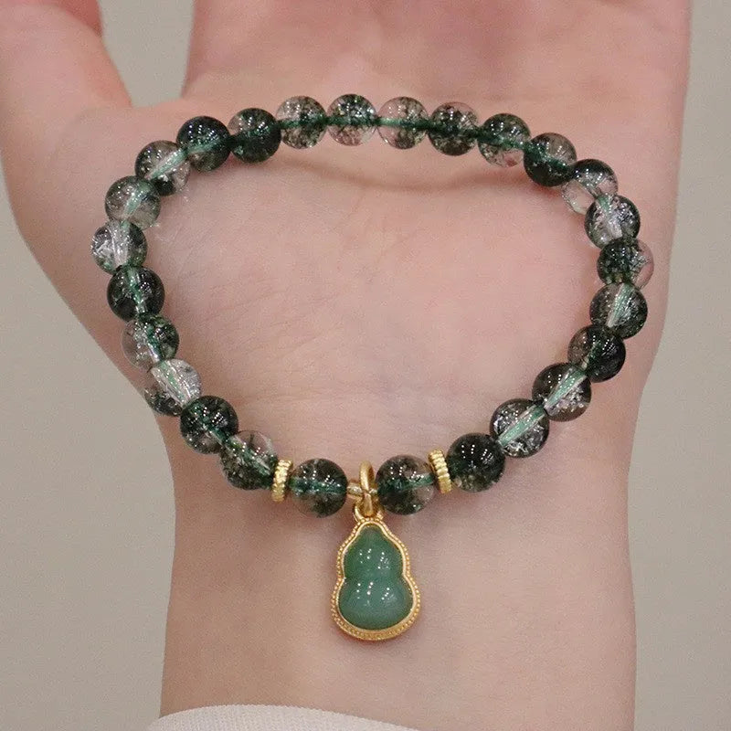 Women's citrine bracelet with green phantom quartz heart charm and pearl accents on a wrist.
