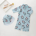 Toddler boy wearing a penguin print long sleeve one-piece swimsuit and matching swimming cap.
