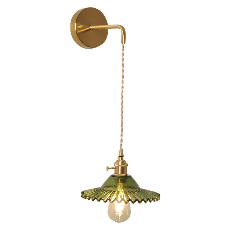Brass wall lamp with an adjustable smoked grey glass lotus shade mounted beside a bed.
