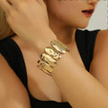 Gold exaggerated elliptical cuff bangle with 4mm band width on a neutral background