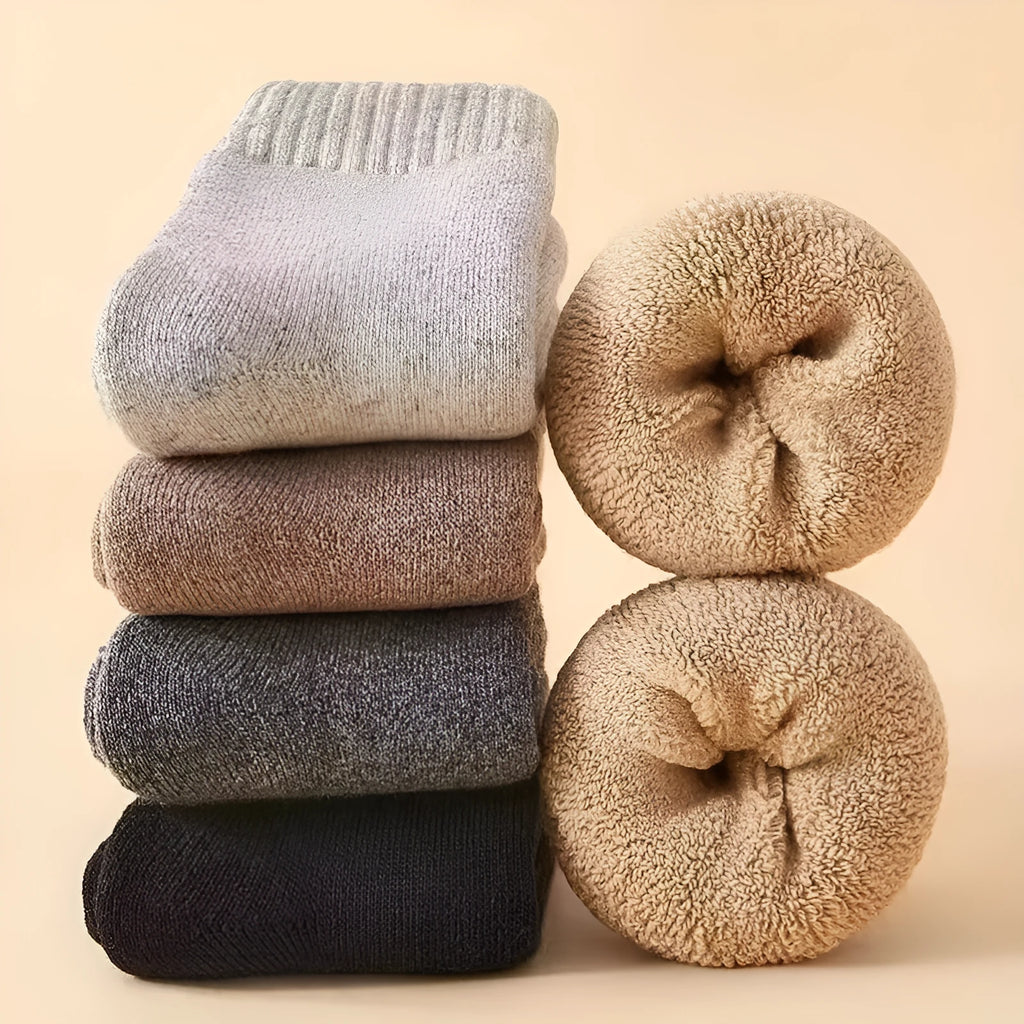 Set of four pairs of solid-colour merino wool socks with reinforced heel and toe on a wooden surface.