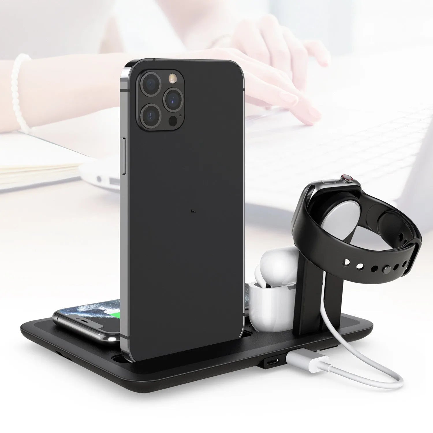 Black desktop wireless charging station with phone on pad and ports for watch and headphones.