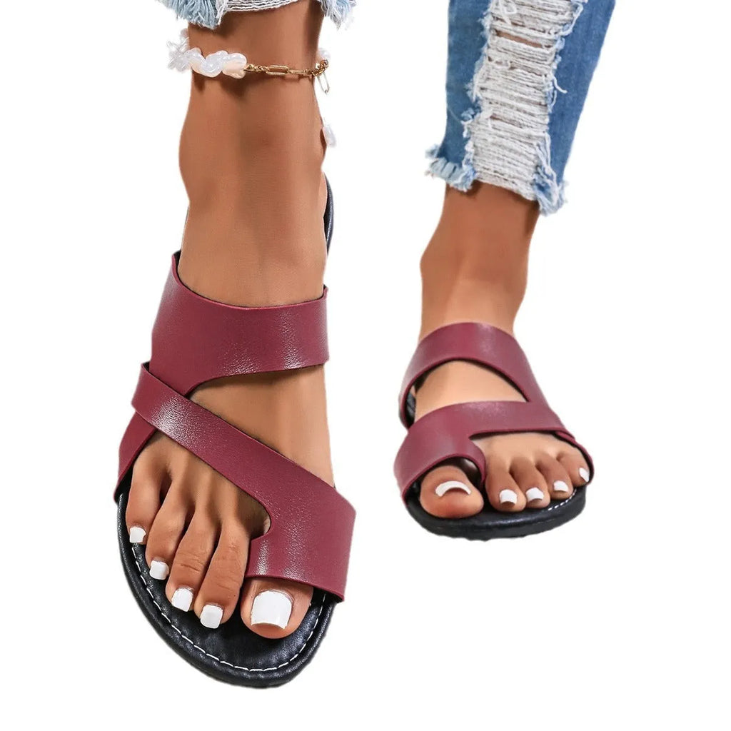 A pair of casual black beach slippers with a one-line design and hollow out details on a sandy background.