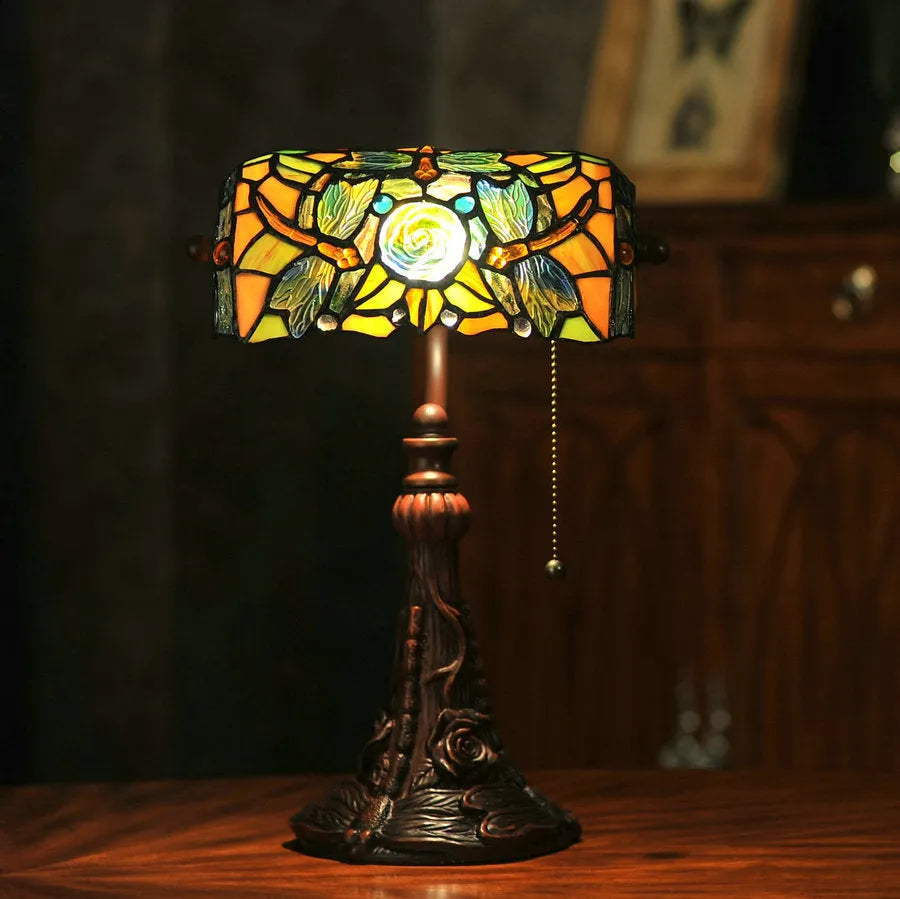 Tiffany style table lamp with coloured stained glass shade on a resin base, shown on a desk.