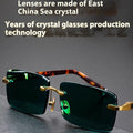 A pair of frameless sunglasses with dark green crystal lenses, shown with a hard protective case and a microfibre cleaning cloth.