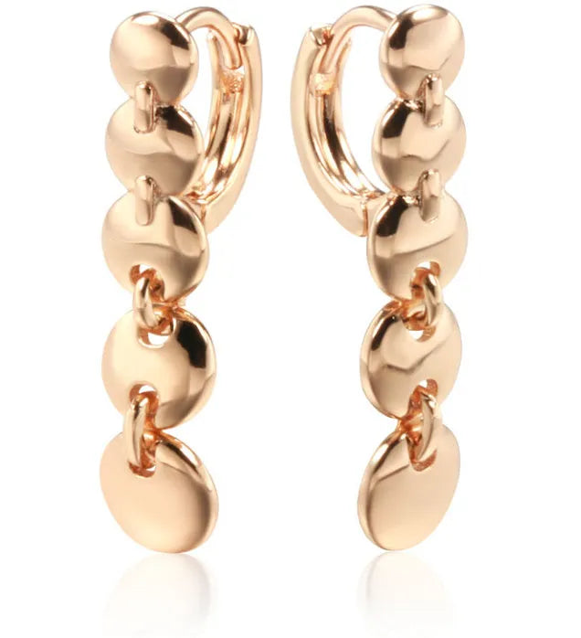 A pair of long, round, woven copper earrings with a gold finish, showing textured detail.
