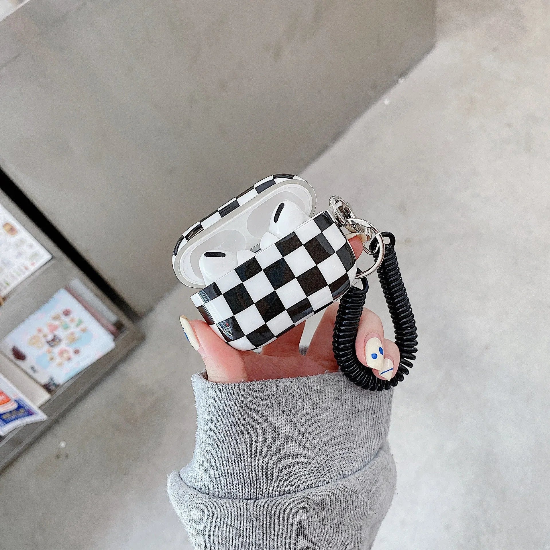 Black and green checkerboard patterned TPU protective case for Apple AirPods with optional lanyard and loop pendant attachments.