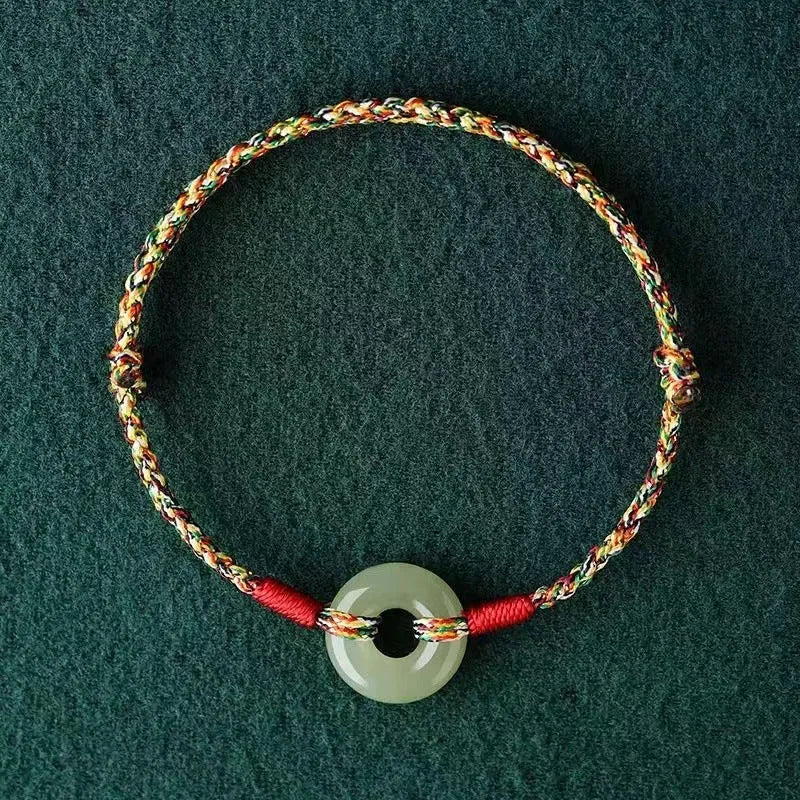 Close-up of a colourful woven rope bracelet with a silver peace buckle clasp on a wrist.