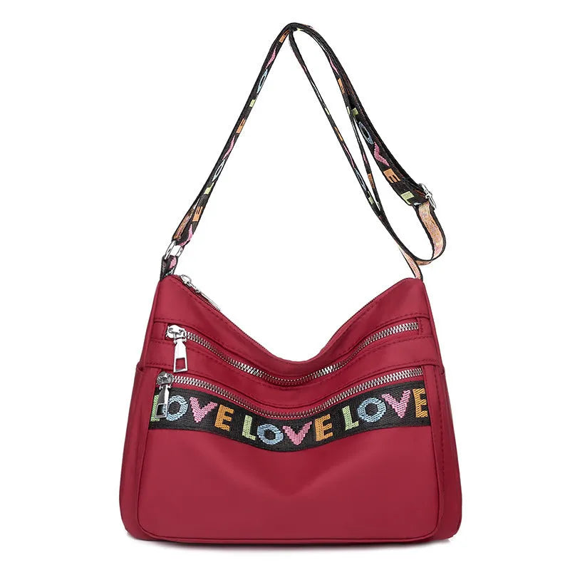 Oxford cloth crossbody shoulder bag in red or black with multi-pocket design, single strap, polyester lining, and letter stitching detail.