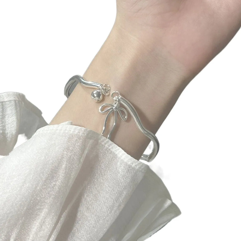 Silver-toned adjustable bracelet with a detailed bow charm on the wrist, showing the opening clasp mechanism.