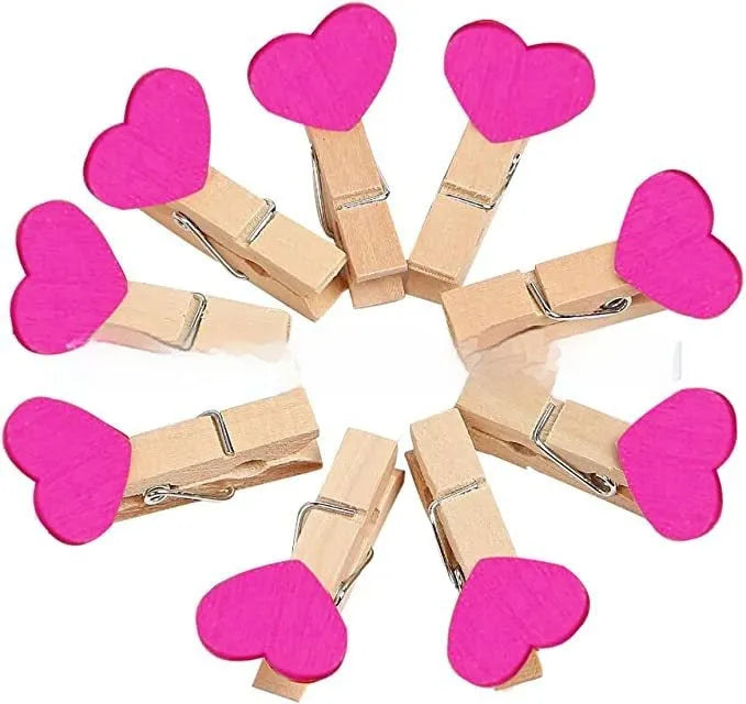 Five small wooden heart-shaped clips in red, pink, white, yellow, and rose colours on a wooden surface.