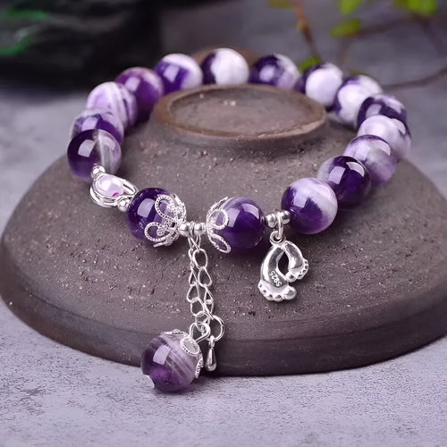 Women's amethyst bracelet with 10mm round purple beads on a wrist.