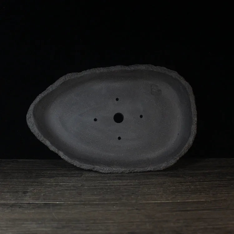 Handmade purple clay flower pot with drainage hole on a wooden floor