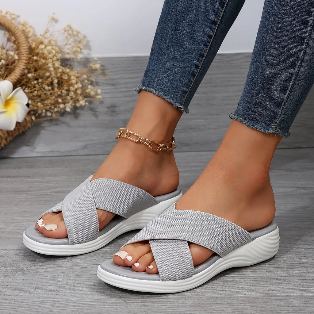 Black women's peep-toe slippers with a cross strap and thick flat rubber wedge sole.