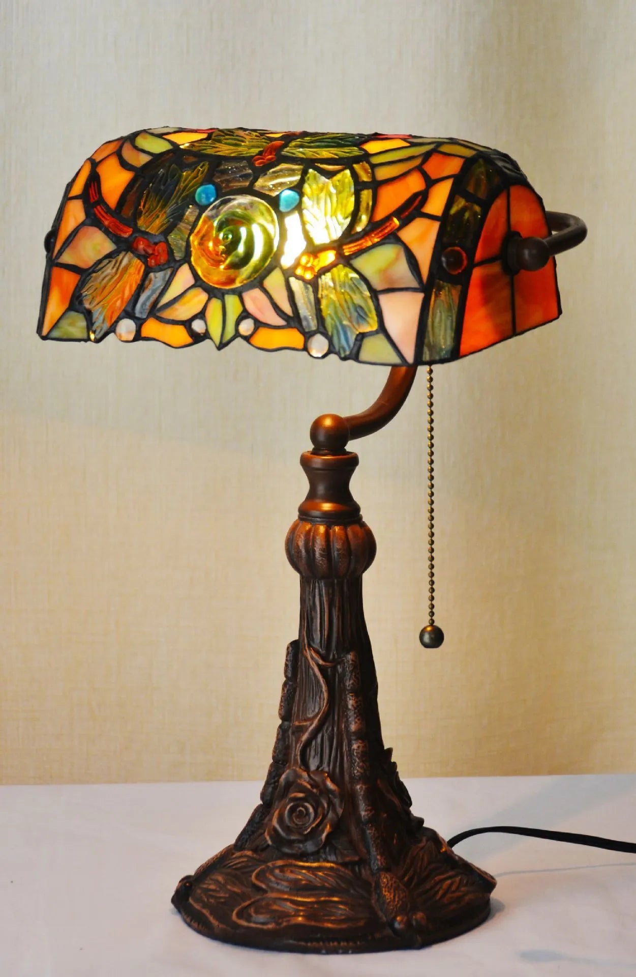 Tiffany style table lamp with coloured stained glass shade on a resin base, shown on a desk.