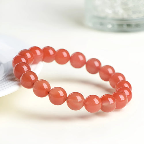 A close-up of a polished cherry red agate bead bracelet on a wrist.
