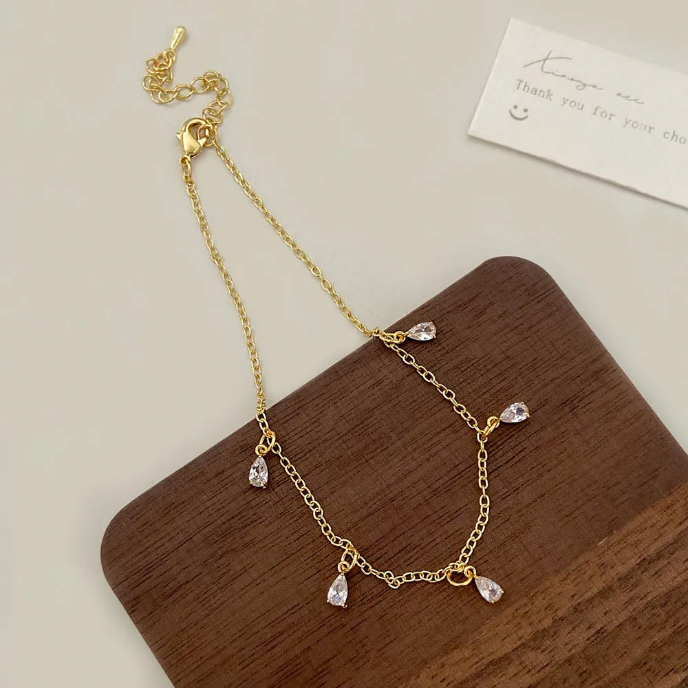 A zircon jewellery set comprising a geometric pendant necklace, stud earrings, and an anklet on a white background.