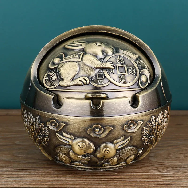 Alloy decorative ashtray in bronze with ornate peacock motif and cigarette extinguishing slot.