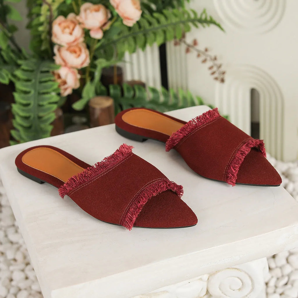Women's solid colour denim flat slippers with a tassel detail on the front.
