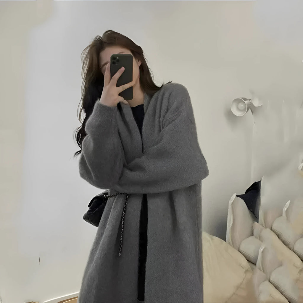 A woman wearing a loose, thick knitted chenille cardigan in a solid colour, showcasing its long sleeves and medium length.
