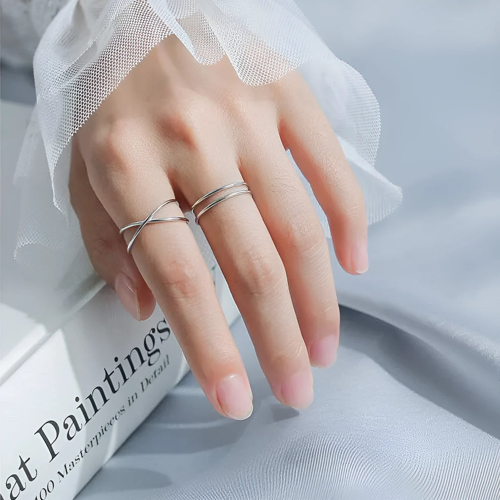 Silver plated geometric cross ring with adjustable opening on a plain background.