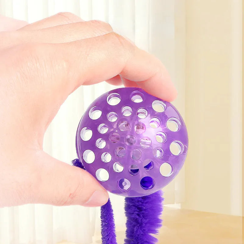 Green bouncy worm-shaped cat toy with a long plush tail on a wooden floor.