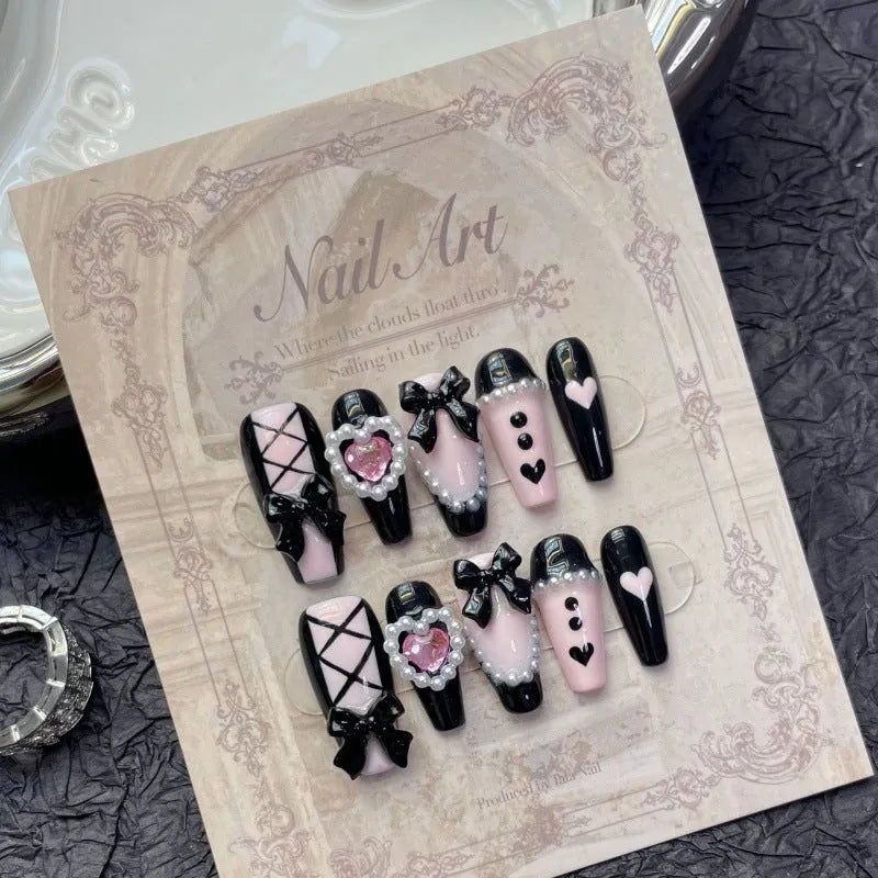 Black false nails with pink hand-painted peach hearts and bow design, shown in a cat's eye style.